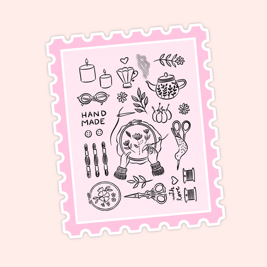 Pink postage stamp style sticker with black line art of embroidery supplies, candles, teapot, florals, scissors, thread, and the word handmade.