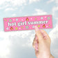 A hand holding a pink bumper sticker that says "hot girl summer" surrounded by daisies, flames, smiley faces, and sparkles.