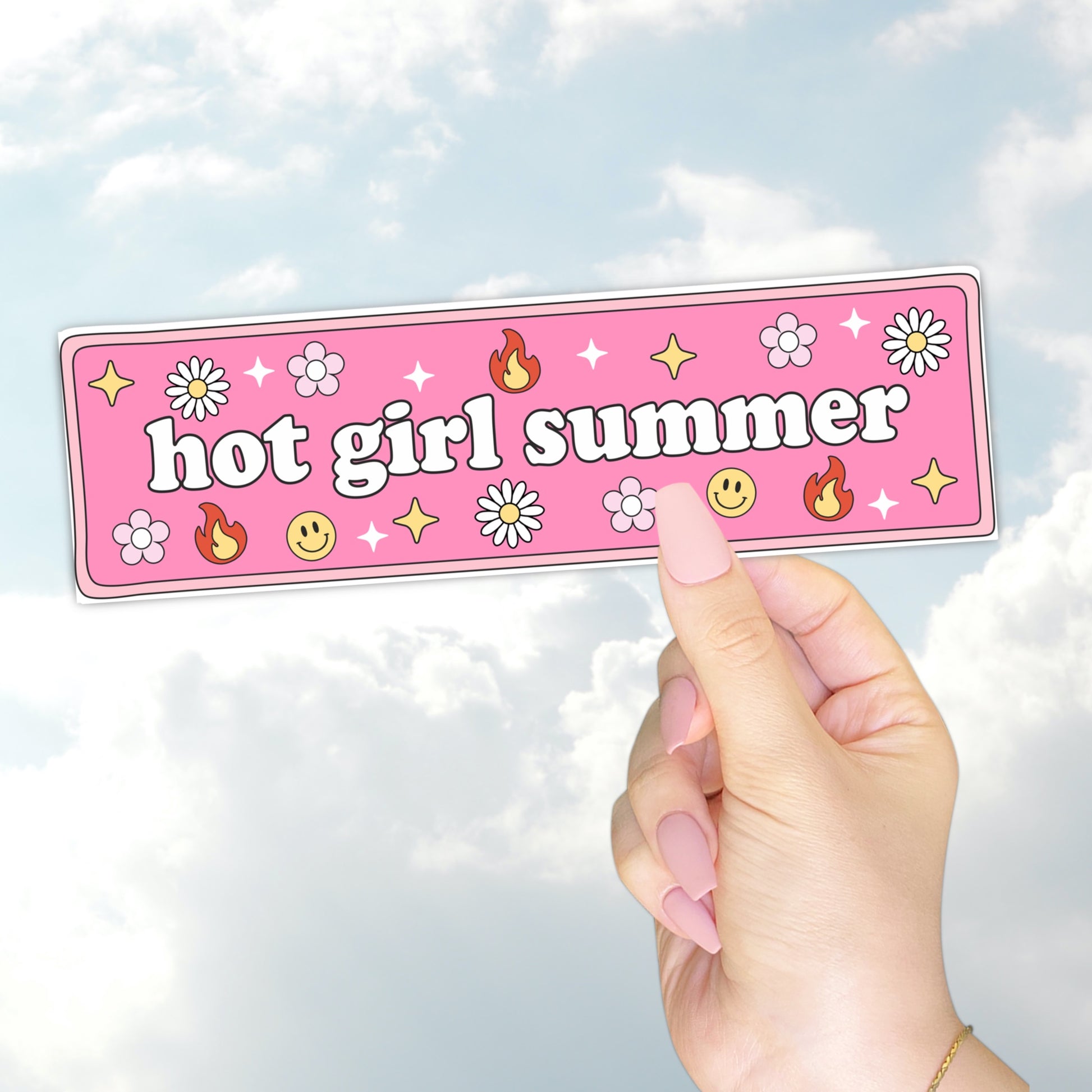 A hand holding a pink bumper sticker that says "hot girl summer" surrounded by daisies, flames, smiley faces, and sparkles.