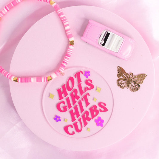 “Girly pink car charm with ‘Hot Girls Hit Curbs’ quote – cute and funny driving accessory for chaotic icons.”