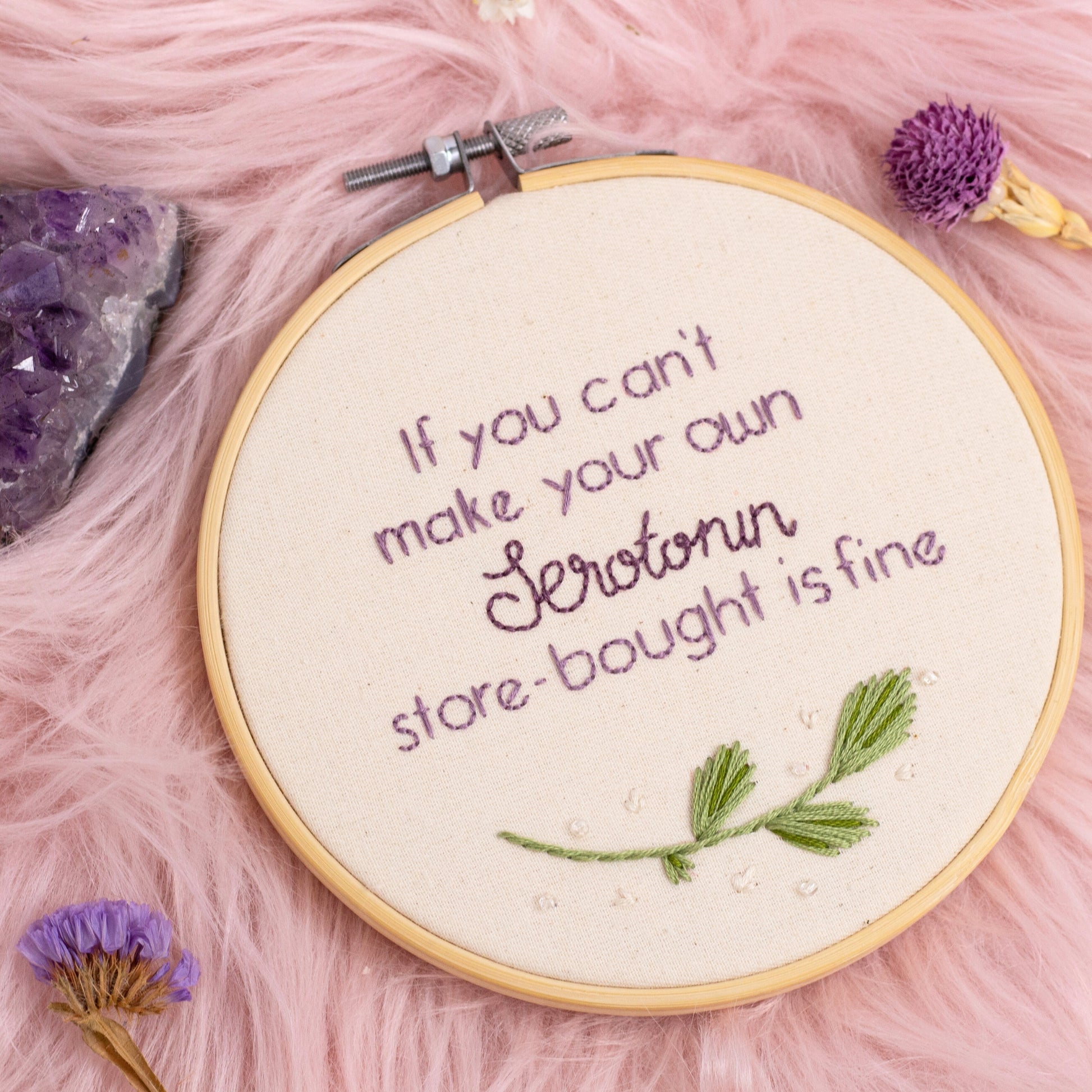 Close up of serotonin quote embroidery hoop with purple lettering and green leaf embroidery in wooden hoop