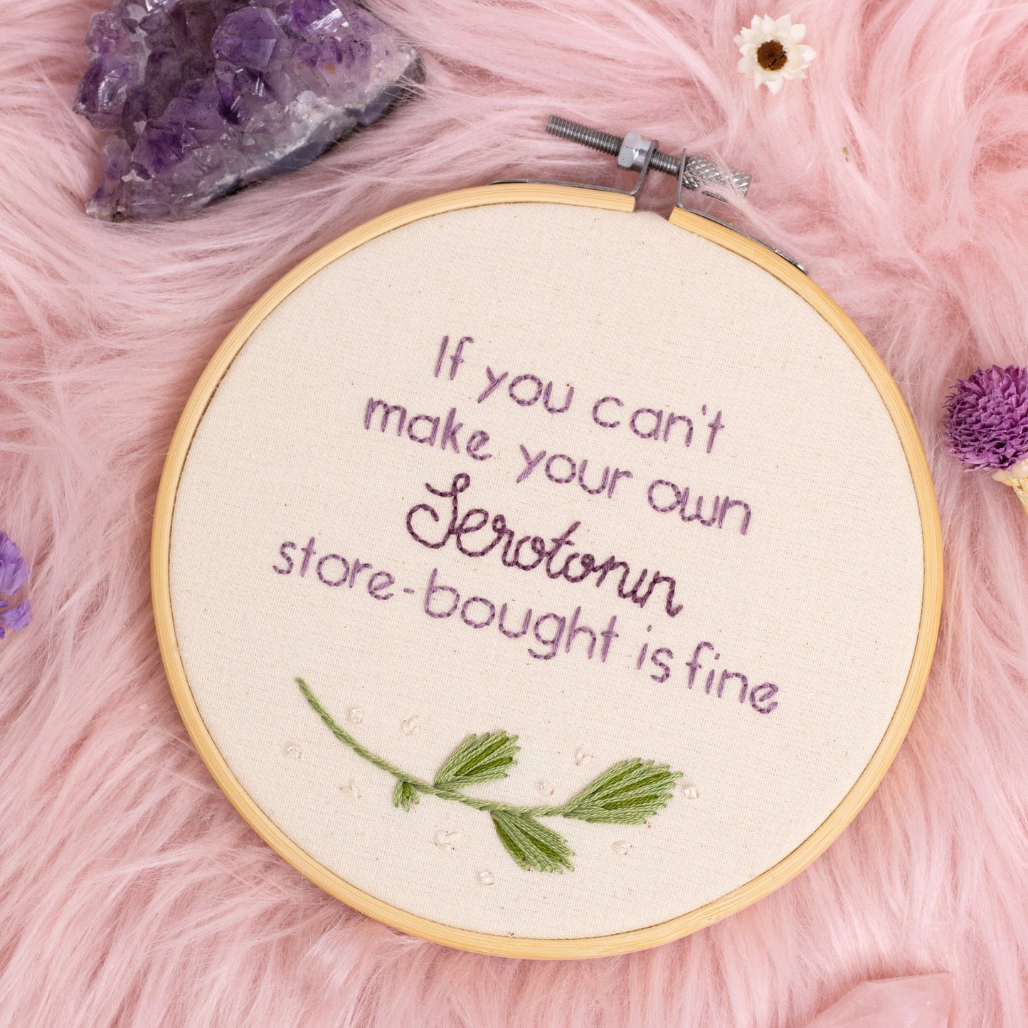 Hand embroidered serotonin quote embroidery hoop wall art on pink background with crystals and dried flowers