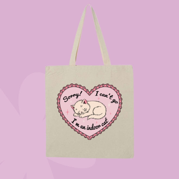 Beige canvas tote bag featuring a sleepy kitten inside a pink heart with text that says Sorry! I can’t go, I’m an indoor cat.