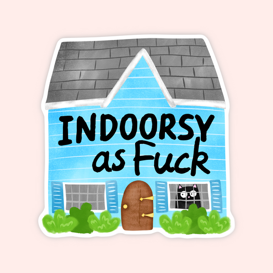 A die-cut sticker featuring a cartoon house with the text 'INDOORSY as Fuck' in black lettering. The house has light blue siding, a gray shingled roof, a brown door, green bushes, and a black cat peeking out of one window.