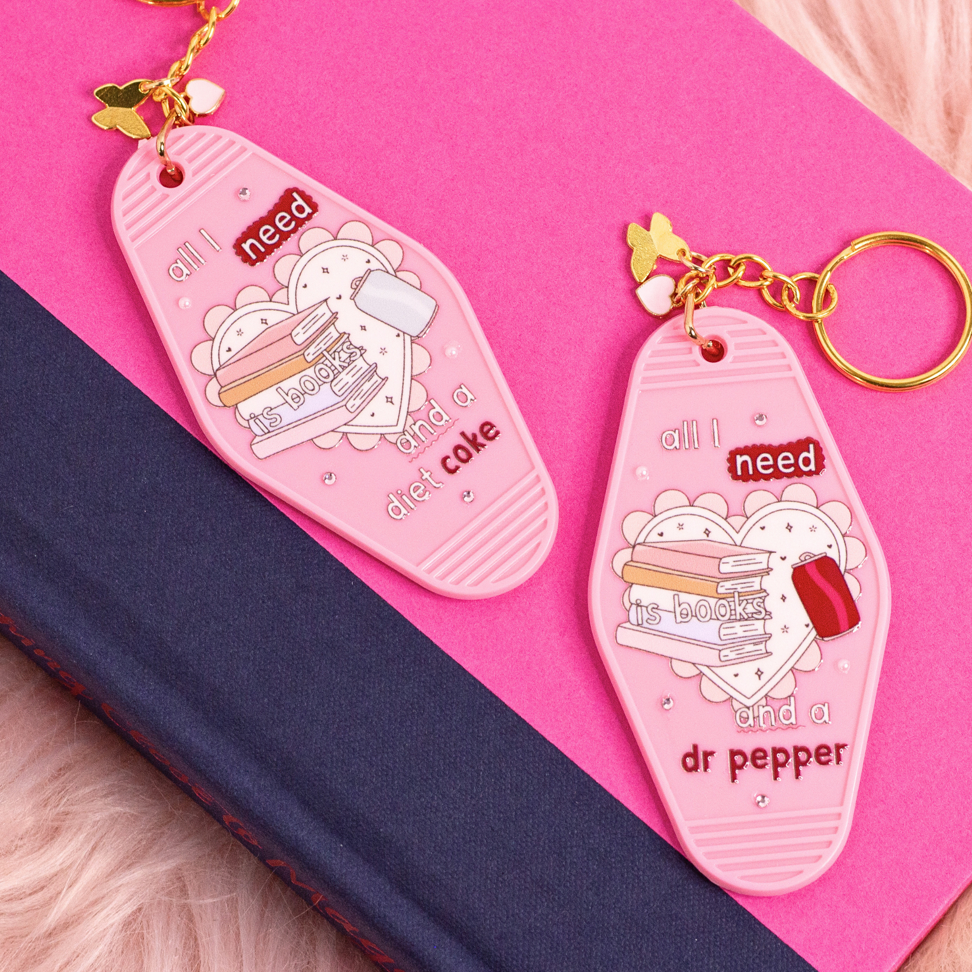 two pink motel style keychains with books illustration showing dr pepper and diet coke variants styled on books
