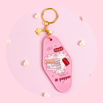 pink motel style keychain with books illustration and “all i need is books and a dr pepper” text, rhinestones and gold key ring on pink background