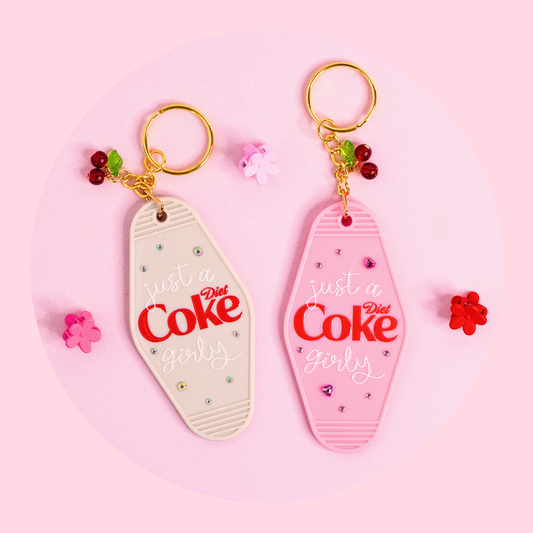 pink and grey retro motel style keychains with “just a Diet Coke girly” text, rhinestones and cherry charms on pink background