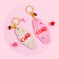 two girly motel style keychains in pink and grey with cherry charms styled on pink surface with small flower clips