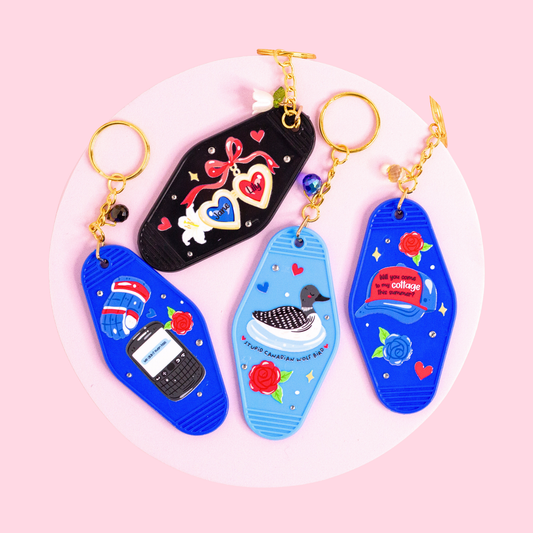four retro motel style keychains inspired by hockey romance book, featuring blue, black and light blue designs with hearts, flowers, duck illustration and text details