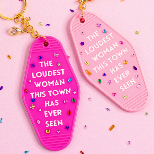 pink and light pink motel style keychains with “the loudest woman this town has ever seen” text, rhinestones and gold hardware on pink background