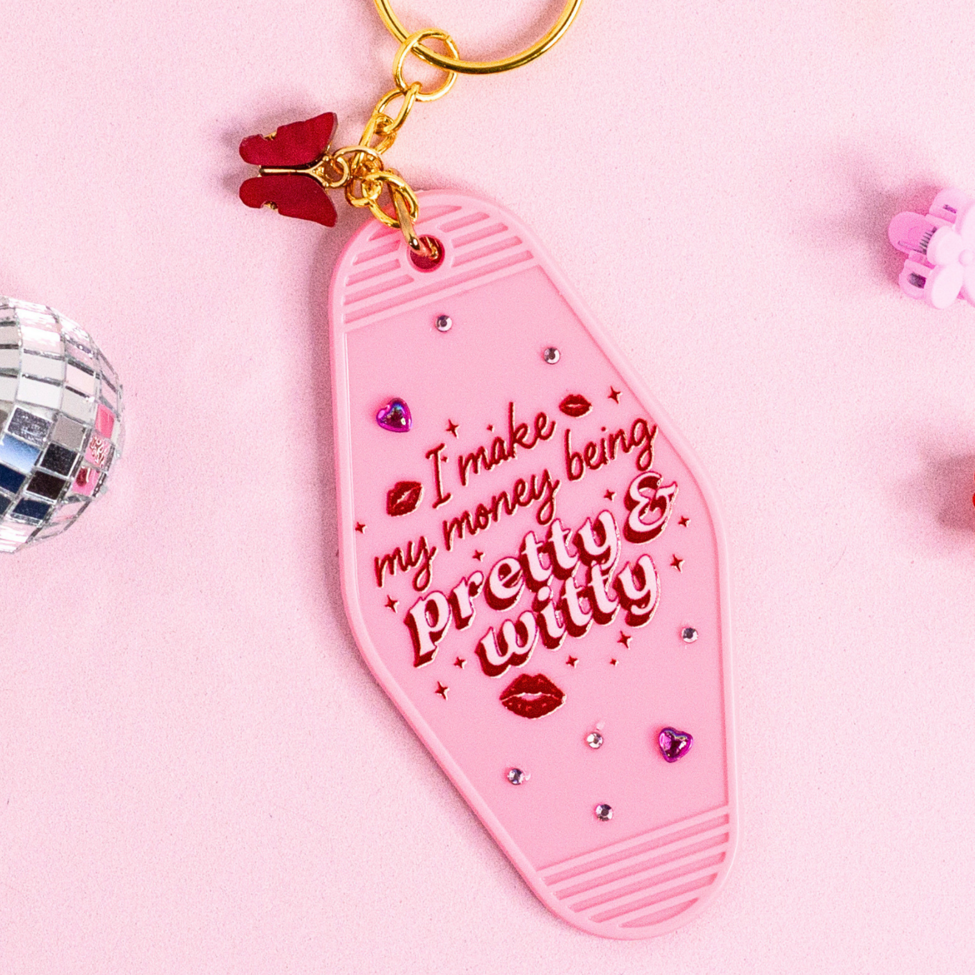 close up of pink retro motel keychain with red lettering “pretty & witty”, rhinestone details and glossy finish with gold hardware