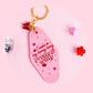 pink motel style keychain with gold key ring and butterfly charm, red text “i make my money being pretty & witty”, rhinestones on pink background with disco ball