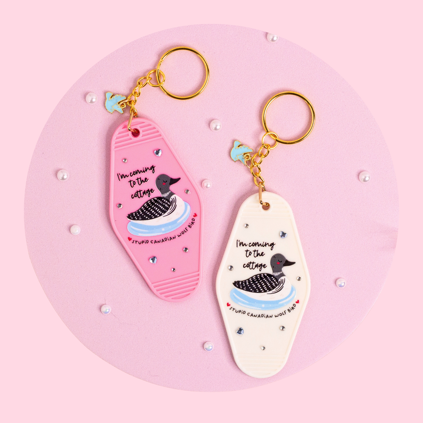 pink and white retro motel keychains with loon design and text, sparkly details and gold hardware styled on soft pink surface