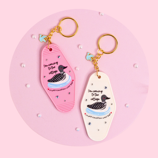 pink and white retro motel keychains with loon design and text, sparkly details and gold hardware styled on soft pink surface