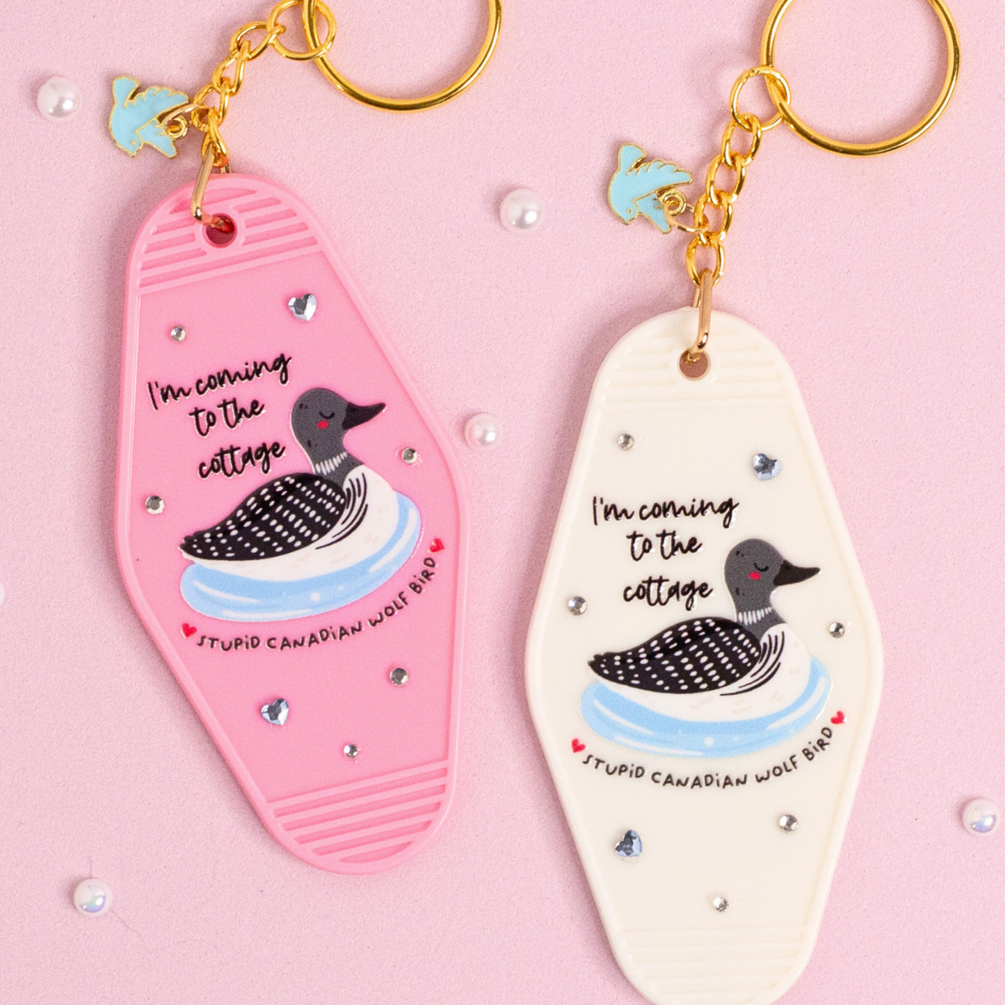 close up of pink and white cottage themed keychains with loon illustration and small heart rhinestones