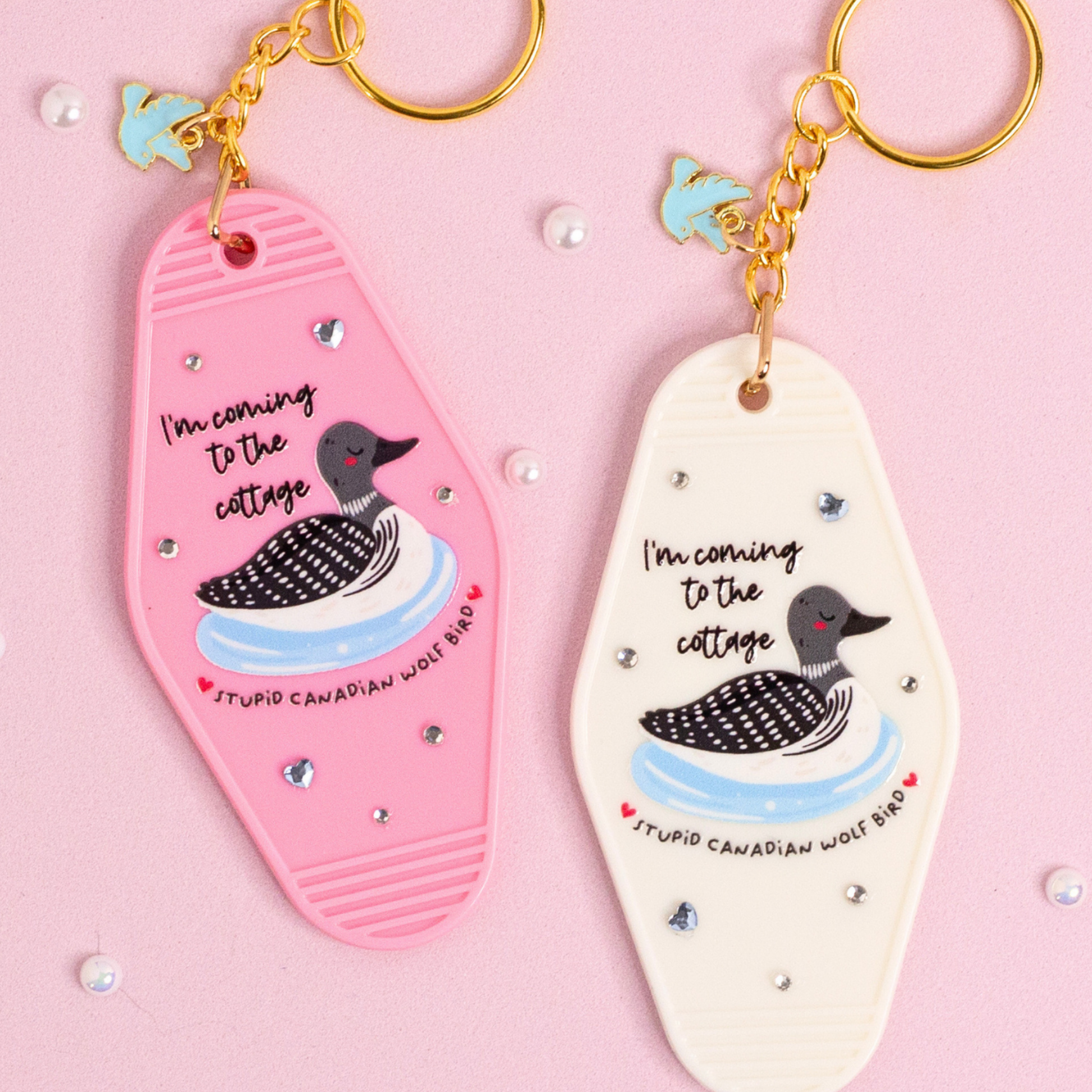 close up of pink and white cottage themed keychains with loon illustration and small heart rhinestones