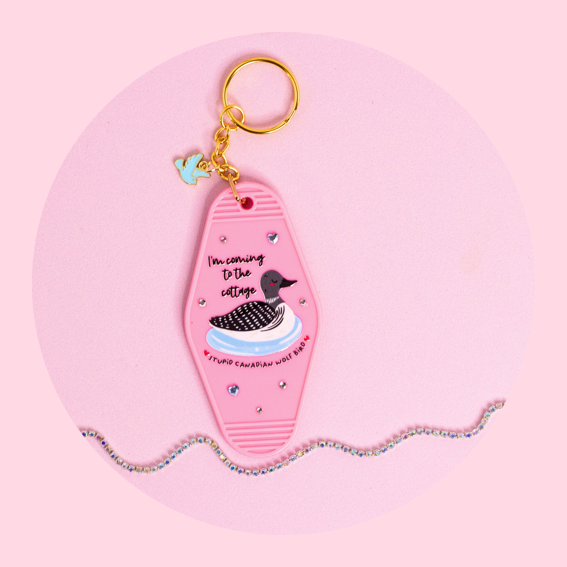pink motel style keychain with loon illustration and “i’m coming to the cottage” text, rhinestones and gold key ring on pink background