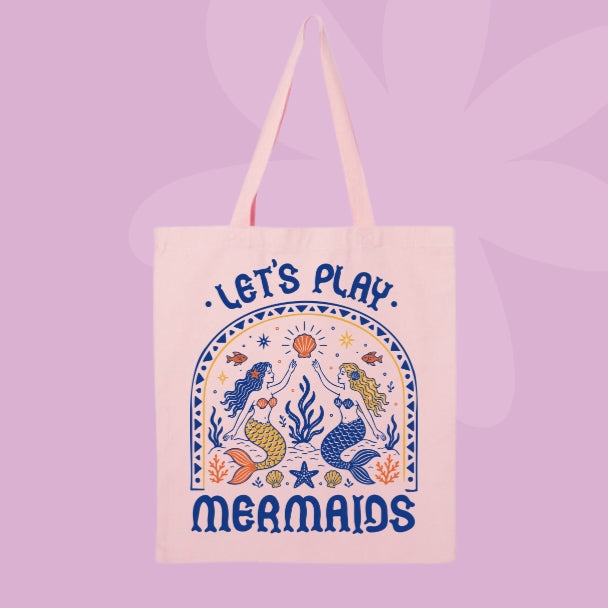 Pink canvas tote bag featuring retro-inspired mermaids, seashells, starfish, coral, fish, and the words Let’s Play Mermaids.