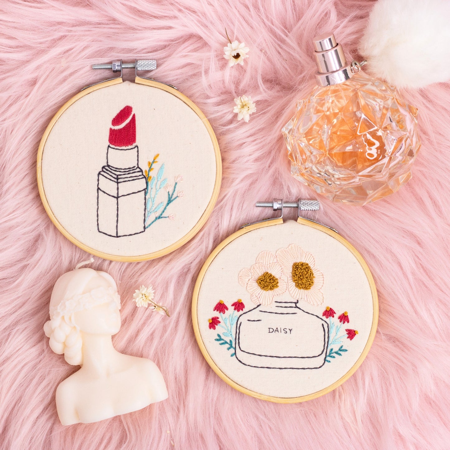 handmade lipstick and floral perfume bottle embroidery hoops on pink faux fur background