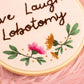 Close-up of handmade embroidery hoop featuring pink stitched flower with green leaves and gold bead accents on neutral fabric