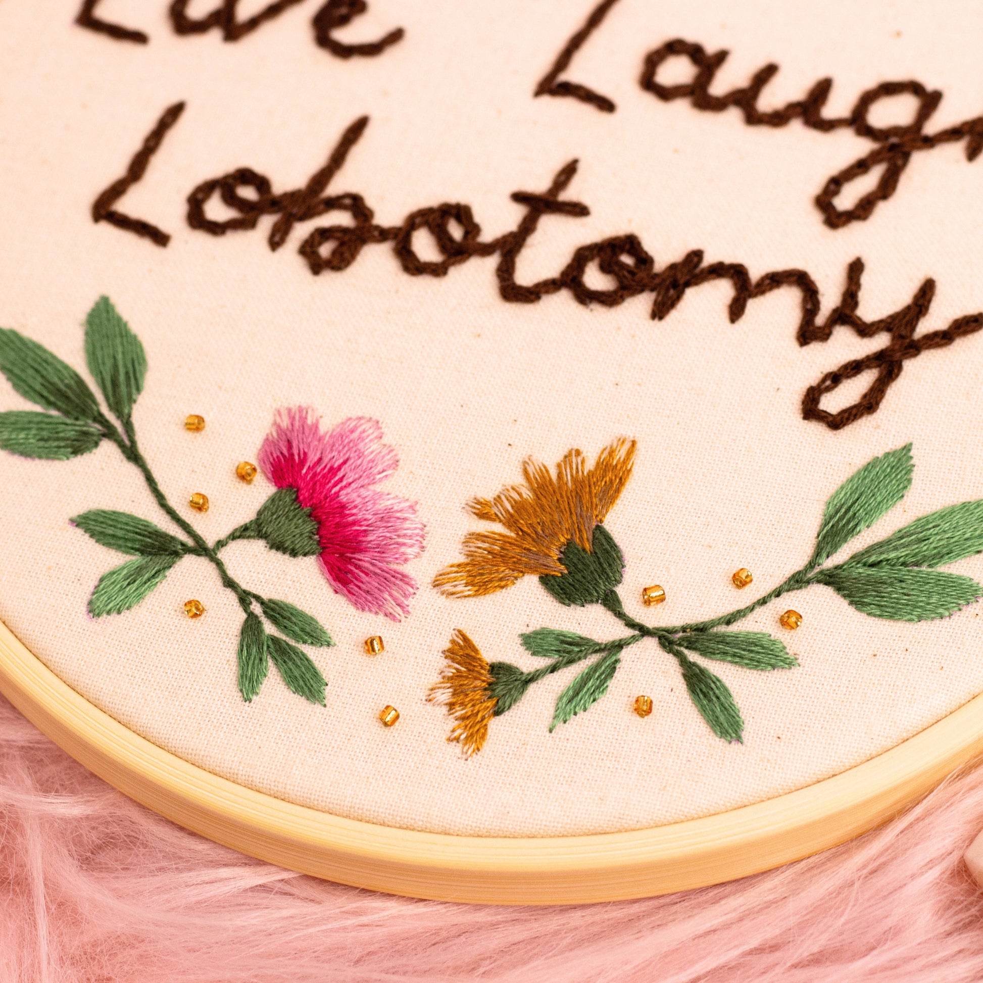 Detailed close-up of embroidered pink and yellow flowers with green leaves and gold bead embellishments