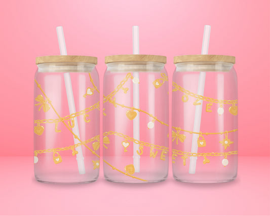 Pink glass can tumbler featuring gold charm chains with hearts, bows, stars, and the words lucky and sweet.