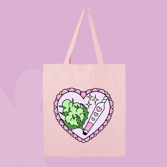 Pink tote bag with a pink heart design featuring green cannabis leaves and a sparkly rolled joint.