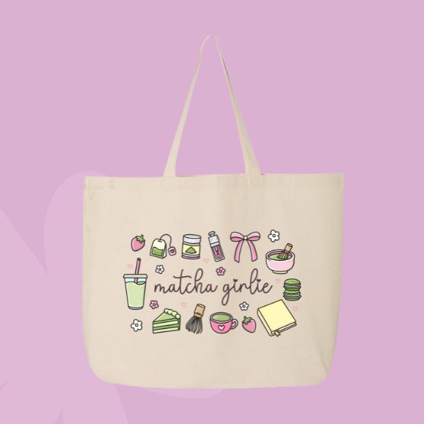 Large beige canvas tote bag featuring the words matcha girlie surrounded by matcha drinks, tea tins, bows, macarons, cake, flowers, and café-inspired doodles.