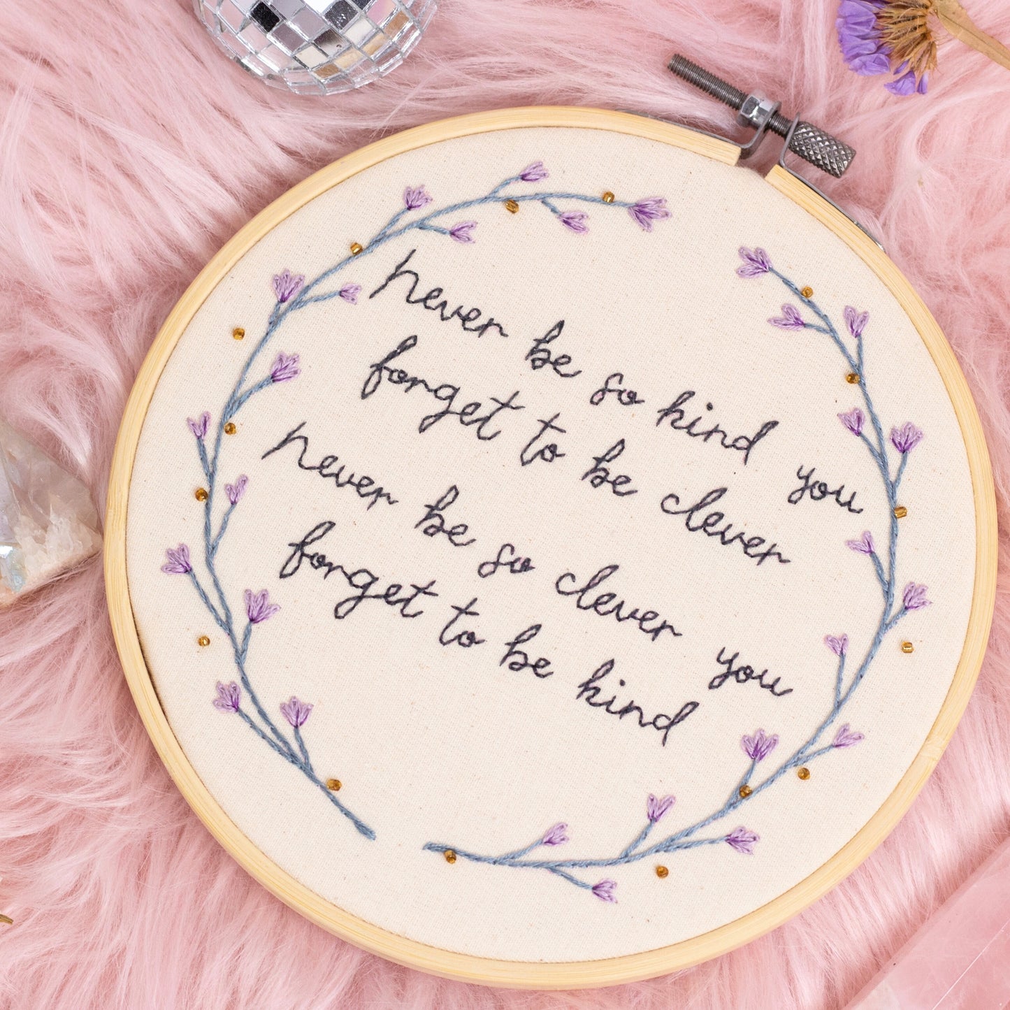 Hand embroidered quote hoop reading never be so kind you forget to be clever surrounded by delicate purple floral wreath