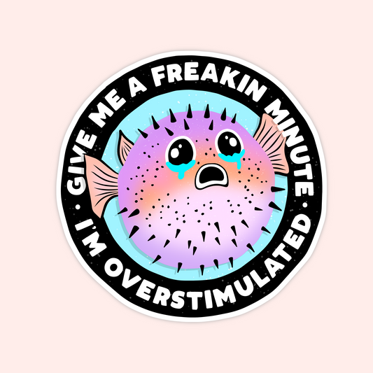 Round sticker featuring a pastel pufferfish with teary eyes and the text "Give me a freakin minute I’m overstimulated."