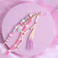 Pink and white purse charm with daisy beads, pastel accents, heart beads, and a purple tassel on a pink clasp.