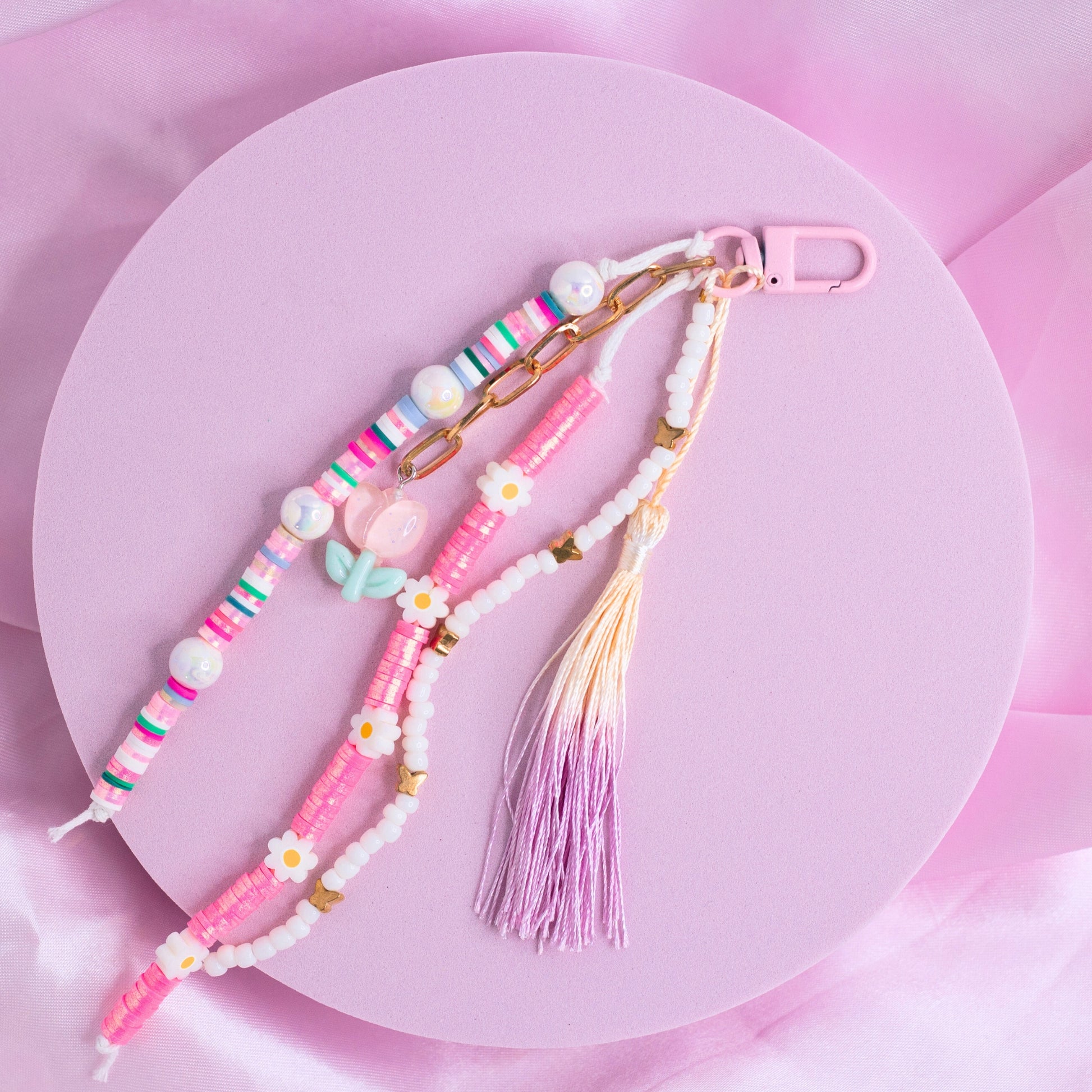 Pink and white purse charm with daisy beads, pastel accents, heart beads, and a purple tassel on a pink clasp.