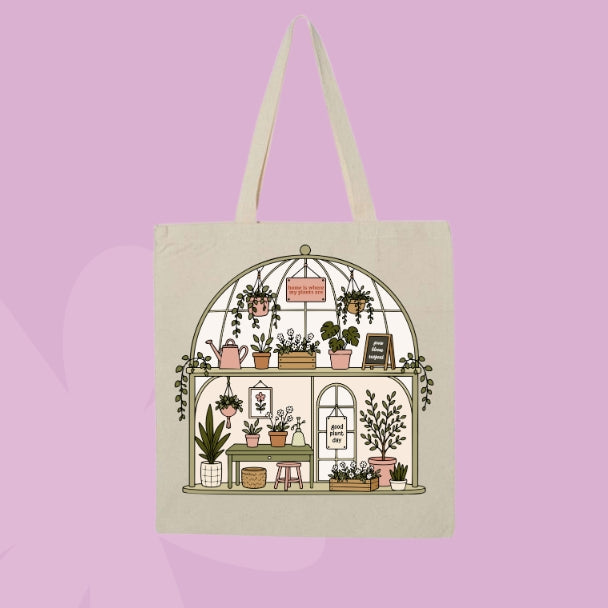Beige canvas tote bag featuring a greenhouse-style plant shop illustration with potted plants, hanging greenery, watering cans, and botanical details.