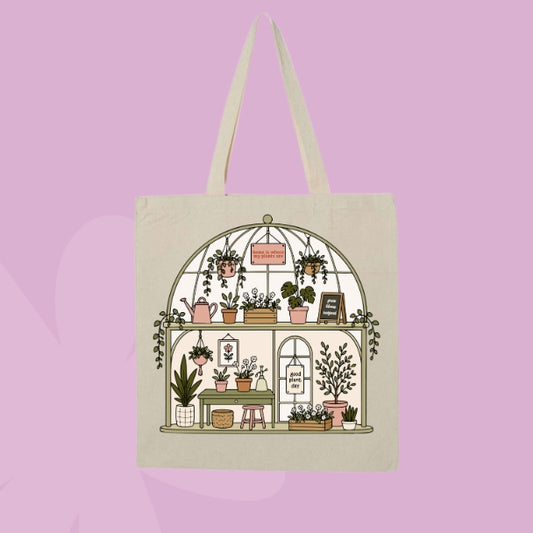 Beige canvas tote bag featuring a greenhouse-style plant shop illustration with potted plants, hanging greenery, watering cans, and botanical details.