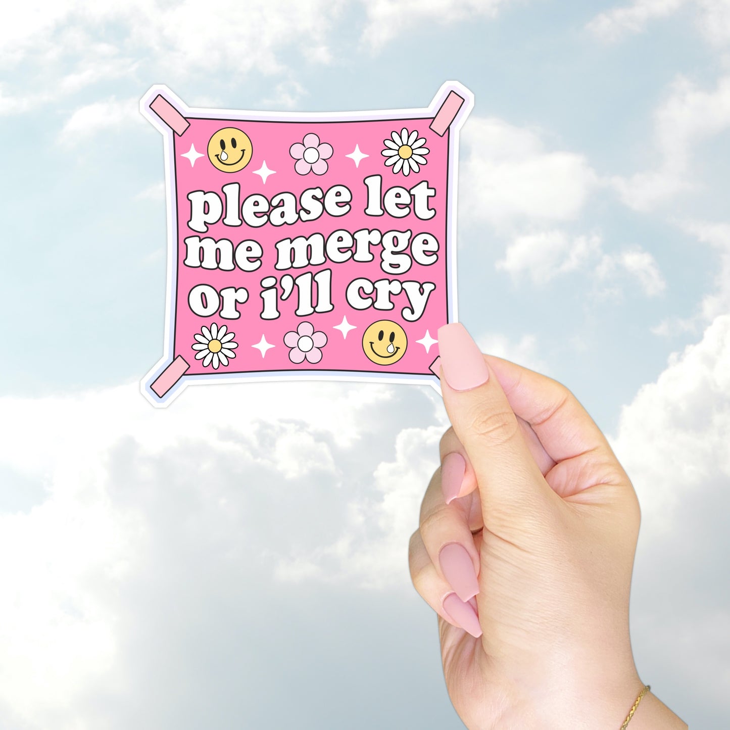 A hand holding a square pink bumper sticker styled like a flag that reads "please let me merge or I’ll cry" with daisies and smiley faces.