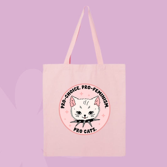 Pink tote bag with a circular design featuring a white cat head and text that says “Pro Choice, Pro Feminism, Pro Cats.”