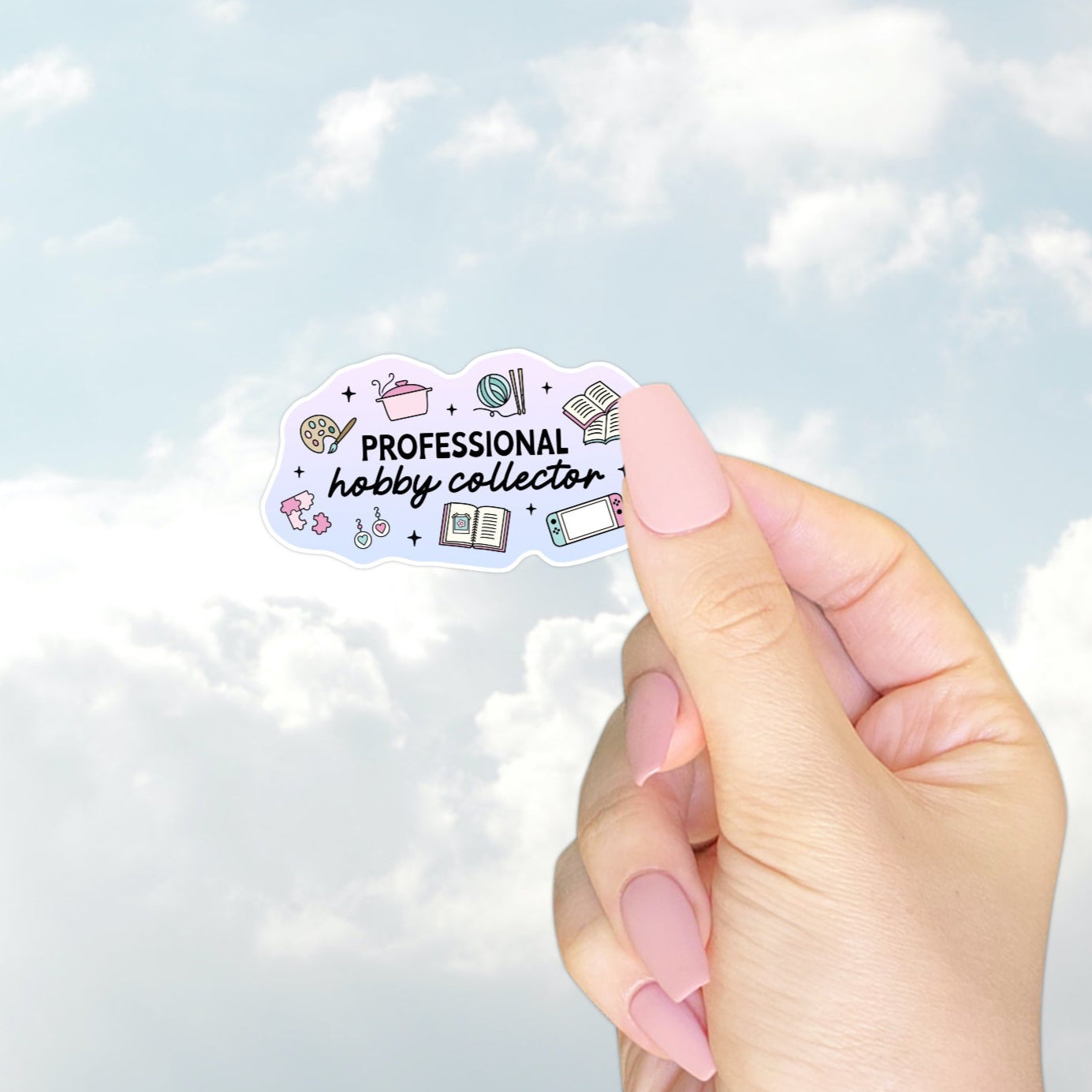 A pastel sticker with illustrations of books, yarn, paint palette, earrings, puzzles, and a Nintendo Switch. Text reads “Professional hobby collector” in mixed fonts, perfect for the creatively chaotic.