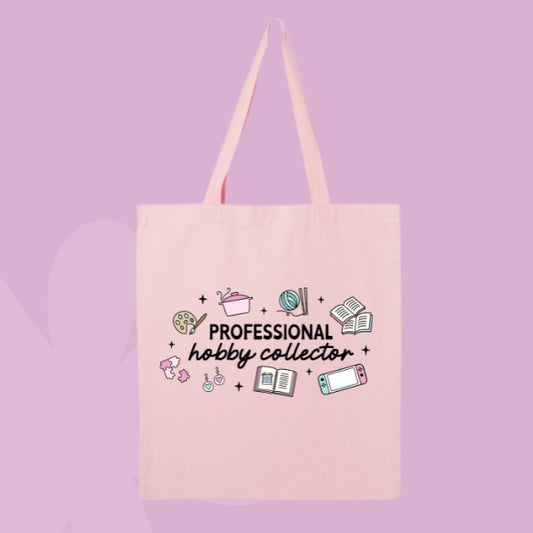 Pink tote bag with doodles of hobbies like painting, knitting, gaming, and reading, with text that says “Professional Hobby Collector.”