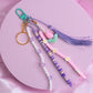 Purple and pink purse charm with striped beads, flower accents, tulip charm, and tassel on a teal clasp.