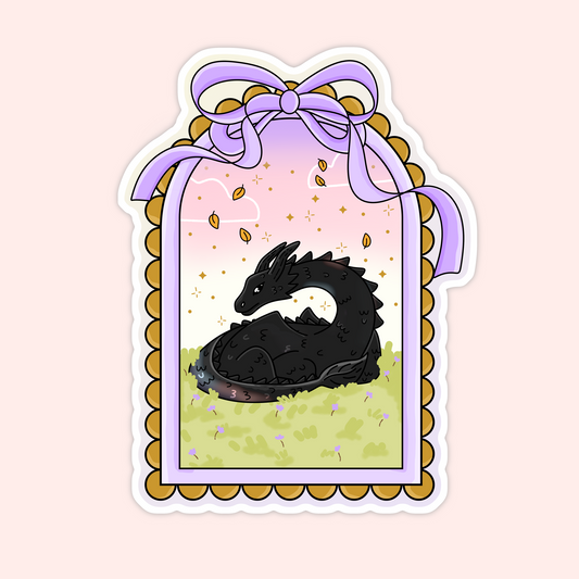 Cute black dragon curled up in a grassy field with a pastel bow frame and falling leaves.