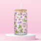 Glass can tumbler with bamboo lid and glass straw featuring pink roses, purple flowers, and green ivy leaves on a pink background.