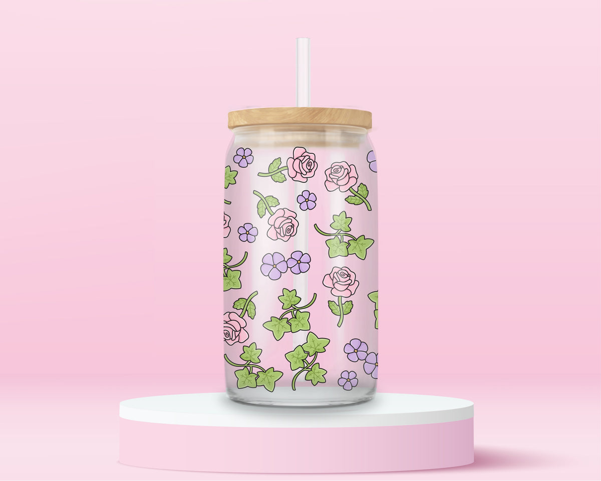 Glass can tumbler with bamboo lid and glass straw featuring pink roses, purple flowers, and green ivy leaves on a pink background.