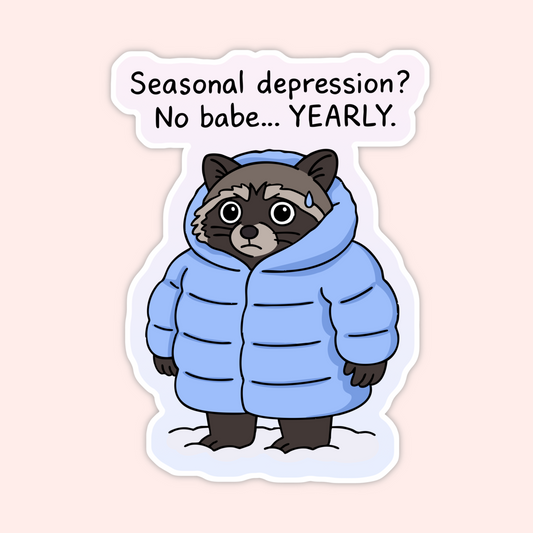 Raccoon wearing oversized blue winter coat standing in snow with text that reads “Seasonal depression? No babe… YEARLY.”