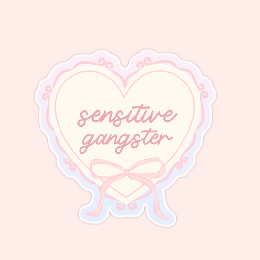 Pastel pink heart-shaped sticker with a bow and text that says “sensitive gangster.”