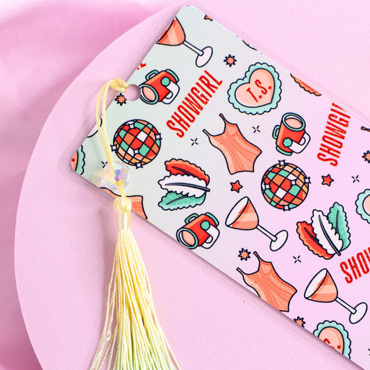 White bookmark with repeating disco balls, cocktails, corsets, and “Showgirl” text, finished with a pastel tassel close up.