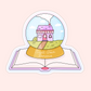 A cozy vinyl sticker featuring a small town romance snow globe resting on an open book. Perfect for romance readers and cottagecore book lovers.