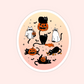 Round Halloween sticker with black cats in ghost costumes, pumpkins, and bats on a pastel gradient background.