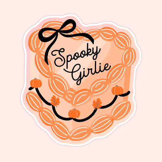 Sticker with the words “Spooky Girlie” inside a scalloped orange retro heart cake decorated with pumpkins, leaves, and a bow.