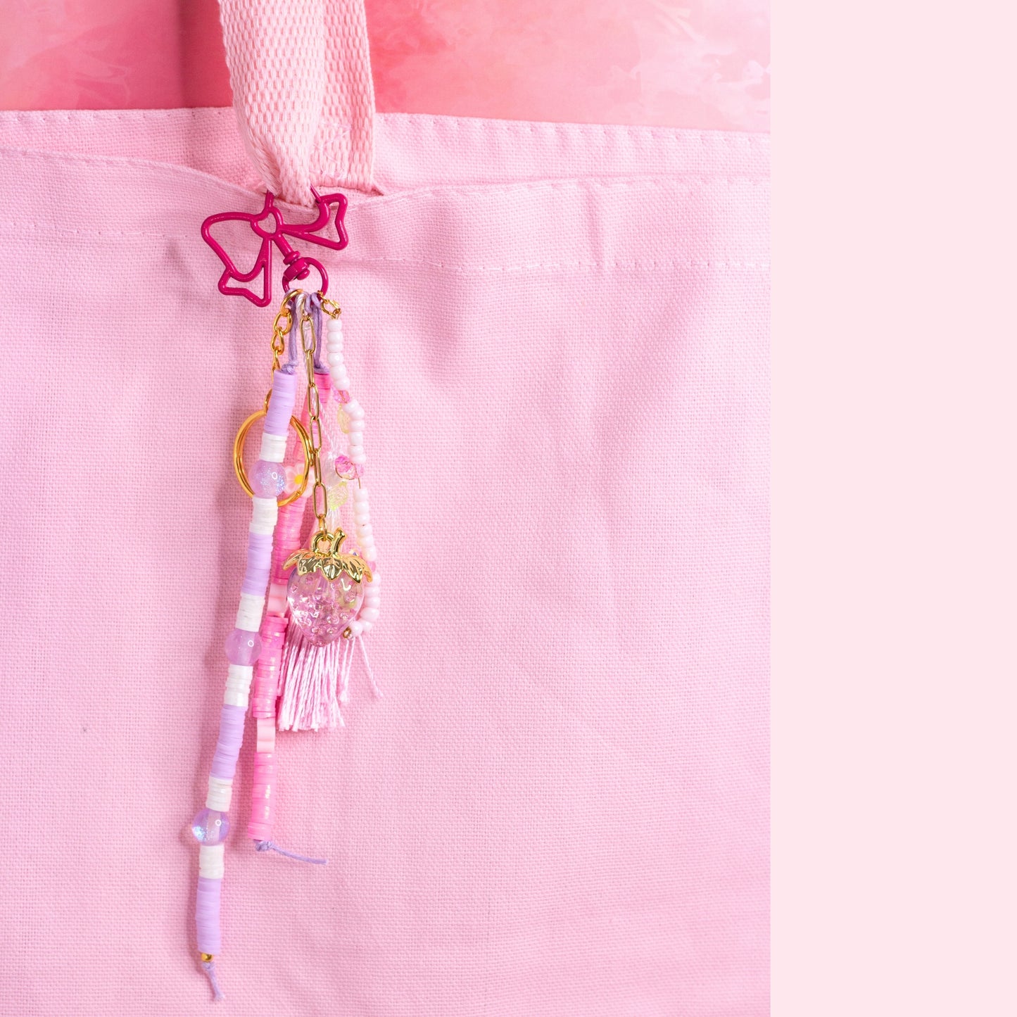 Strawberry beaded purse charm keychain with pink bow clip, pastel beads, and strawberry charm attached to a pink tote bag