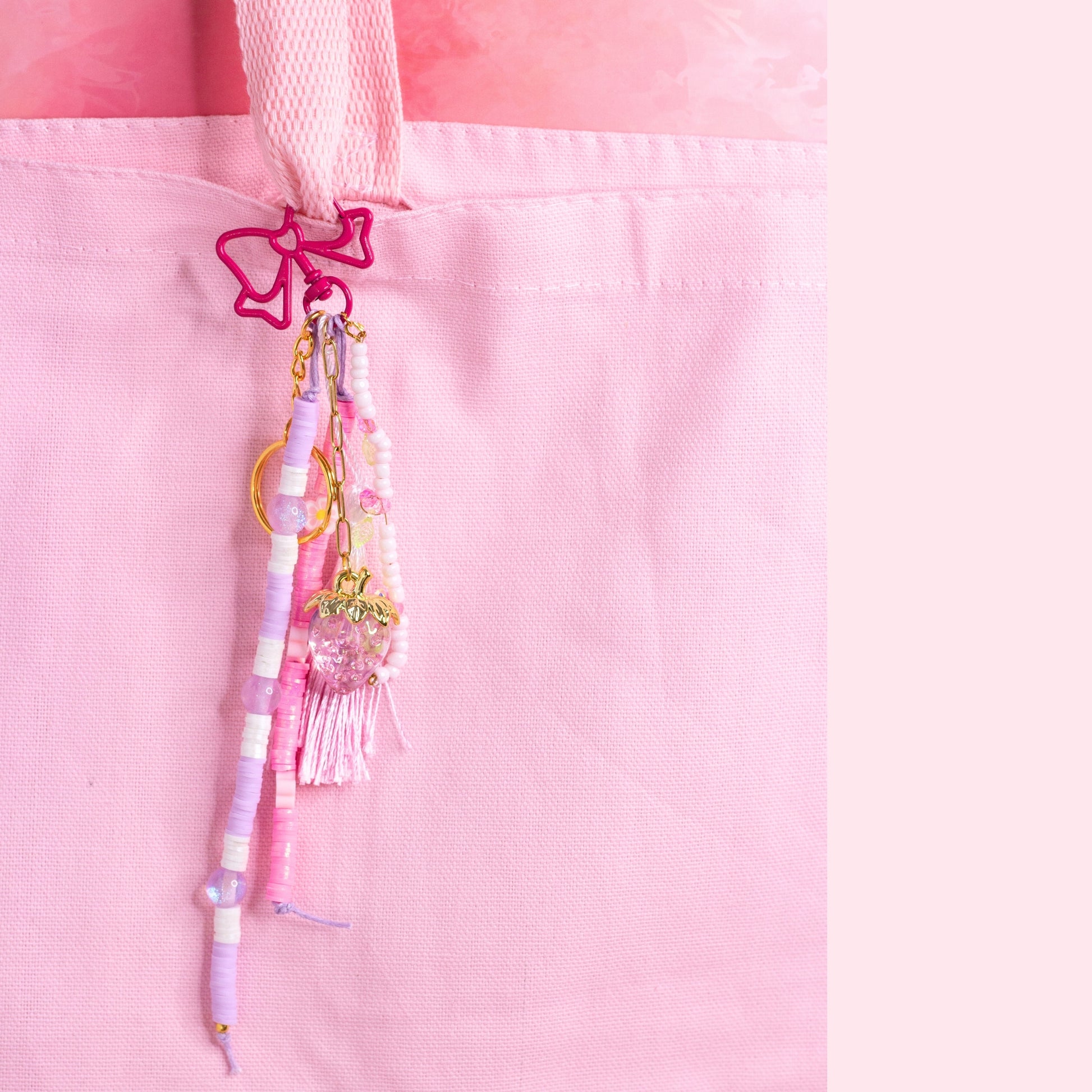 Strawberry beaded purse charm keychain with pink bow clip, pastel beads, and strawberry charm attached to a pink tote bag